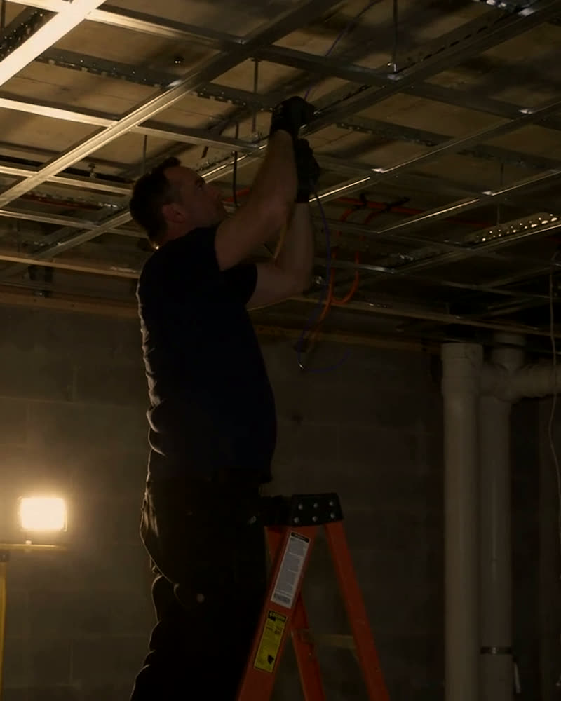 Technician running cable through ceiling grid on a construction site